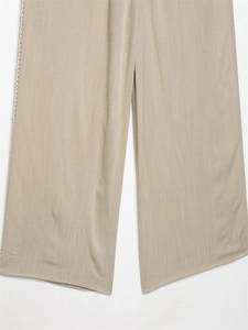 Detail of light beige wide-leg trousers showing fiber texture and side lace trim
