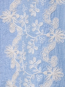 Detailed macro shot of blue textured fabric with intricate white floral embroidery