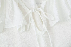 Detailed macro view of white textured chiffon blouse with tie-up closure and ruffled edges