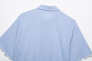 Detail of light blue textured fabric shirt with white scalloped lace cuffs on sleeves