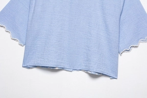 Detail of light blue textured fabric blouse with scalloped cuffs and white lace embroidery