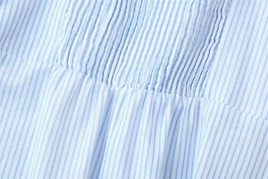 Gros plan sur un tissu à rayures bleues et blanches avec détails de smocks et de plissage