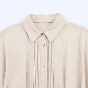 Detail view of beige linen dress featuring vertical pleats and pearlescent buttons