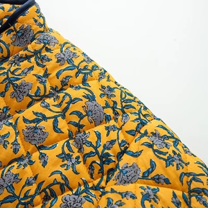 Detailed macro view of yellow floral quilted jacket featuring blue flower patterns and stitching