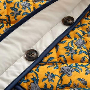 Macro detail of floral quilted jacket showing blue piping and brown textured buttons