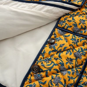 Detail of yellow floral quilted jacket with navy trim and brown wooden button