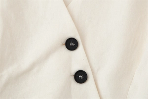 Close-up of black buttons and woven texture on a beige sleeveless two-piece set