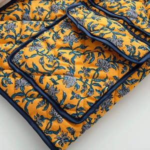 Detail of yellow floral quilted fabric with diamond stitching and dark blue piping edge
