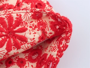 Detail of red floral embroidery and eyelet hollow design on pink fabric surface