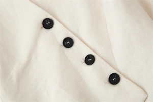 Detail of four black buttons and cream cotton-linen texture on a sleeveless vest