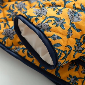 Detail of yellow floral quilted jacket featuring navy satin edge binding and contrast print