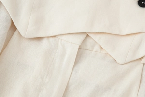 Detailed close-up of cream textured cotton linen fabric with classic collar and black button