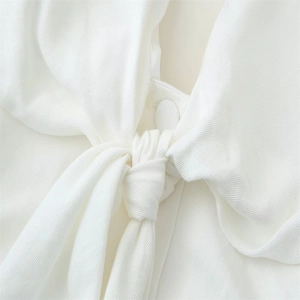 Detail shot of white woven fabric featuring a twisted knot and fabric-covered button