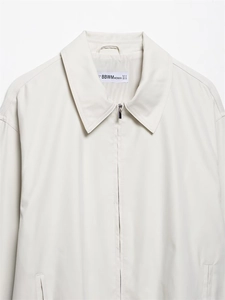 Detail of a minimalist cream bomber jacket featuring a silver zipper and lapel collar