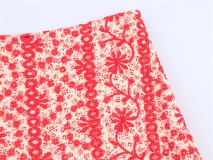 Detail of red floral eyelet embroidery on beige cotton fabric with intricate patterns
