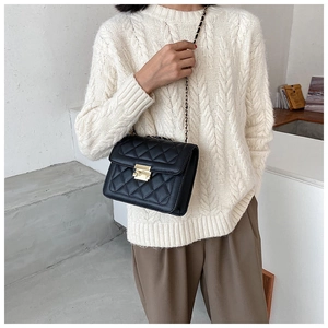 Detail of a black quilted crossbody bag with gold chain strap worn by a model