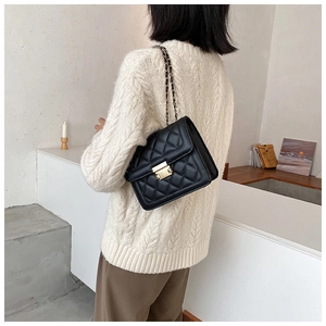 Woman in white sweater wearing a black quilted chain crossbody bag with gold hardware