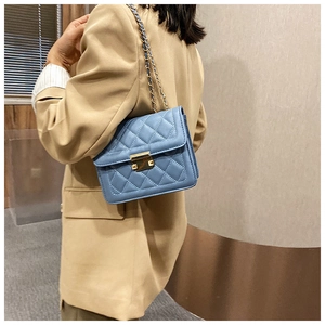 Blue quilted leather chain bag with metallic clasp worn over a beige suit blazer