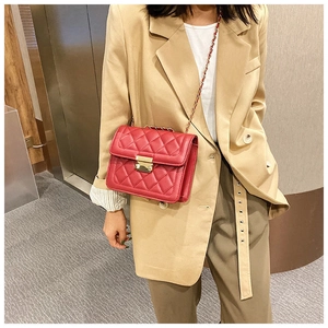 Close-up of red quilted crossbody bag with gold chain strap on a khaki blazer