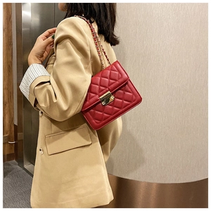 Quilted red crossbody bag with golden chain strap and buckle shown on beige blazer