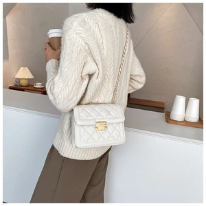 Detail view of a white quilted crossbody bag with gold chain strap and metal lock closure
