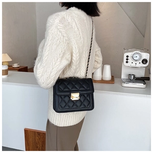 Classic black quilted leather crossbody bag with golden chain strap on a white sweater