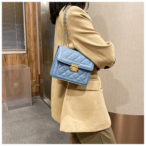 Detail view of a blue quilted crossbody bag with gold lock and chain strap on a model