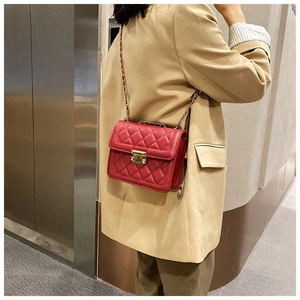 Detail of red quilted crossbody bag with golden chain strap on a khaki blazer