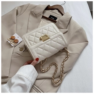 Detail shot of quilted pattern white crossbody bag with gold metal buckle and chain strap