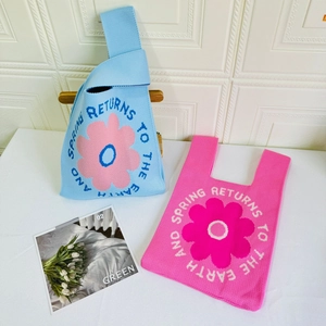 Close-up of knit tote bags with floral patterns and English text on a wooden stand