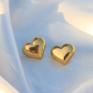 Detail of 3D gold heart earrings on white silk with elegant polished metal finish