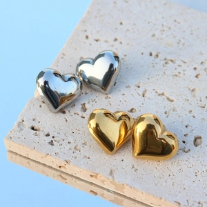Polished gold and silver heart studs displayed on beige stone with mirror reflection