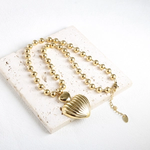 Detailed macro view of gold stainless steel shell-textured heart pendant and bead chain