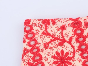 Close-up of intricate red floral embroidery and eyelet cutouts on light pink fabric