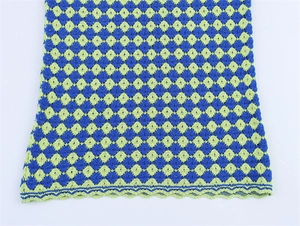 Detailed macro view of the blue and lime green checkered crochet knit fabric and scalloped edge