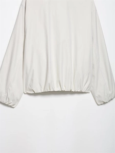Detail of the elastic ribbed hem and smooth fabric of the light beige bomber jacket