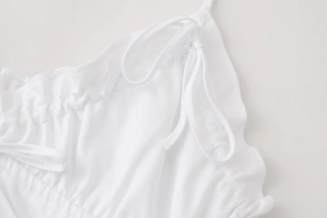 Detail view of adjustable tie shoulder straps and ruffled neckline on a white dress