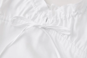 Detailed close-up of a white dress showing fine gathered fabric and minimalist bow tie-up