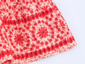 Detail of red floral embroidery and delicate broderie anglaise on pink fabric