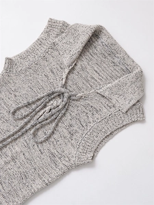 Detail of knit vest showing large lapel and drawstring tie on textured grayscale fabric