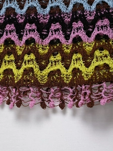 Detail of colorful hand-crocheted wavy pattern with hollow lace and small tassels