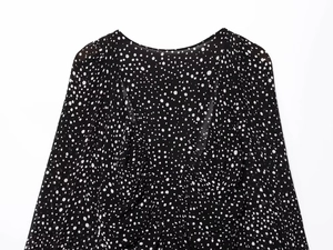 Close-up detail of polka dot chiffon fabric with V-neckline and elegant pleats on black shirt