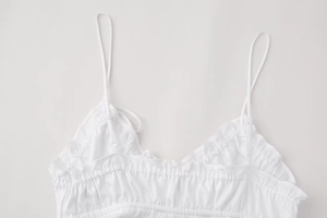 Detailed macro view of white camisole with thin spaghetti straps and delicate pleated neckline
