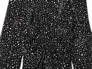 Detailed view of white polka dots on black chiffon fabric with V-neckline pleats