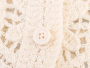Detailed macro view of the cream crochet knit fabric with a matching button closure