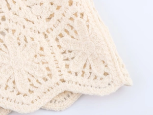 Close-up detail of cream crochet knit top with intricate floral openwork and wavy scalloped edge