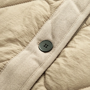 Macro detail of khaki quilted jacket featuring herringbone tape edge and black button