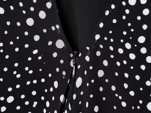 Detailed view of women's black polka dot dress with V-neck and hidden zipper closure
