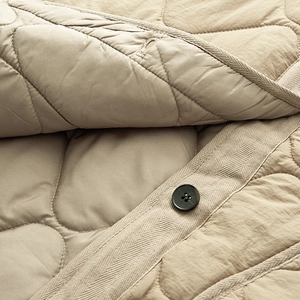 Close-up of khaki quilted cotton jacket featuring black buttons and herringbone tape binding