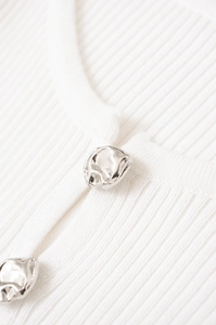 Close-up of white ribbed knit fabric featuring irregular silver liquid metal buttons